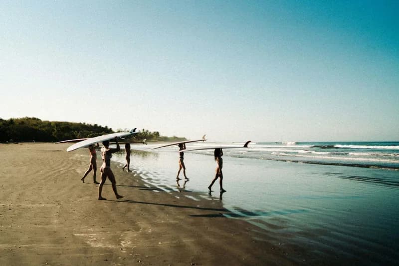 Guests carrying a longboard along Playa Grande beach